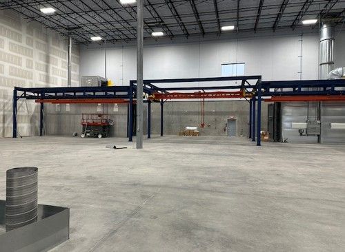 Large empty industrial space with overhead conveyor system and concrete floor.