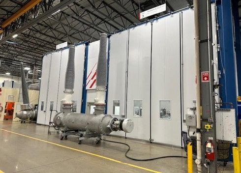 Large industrial paint booth in a factory setting, with attached equipment and venting tubes.