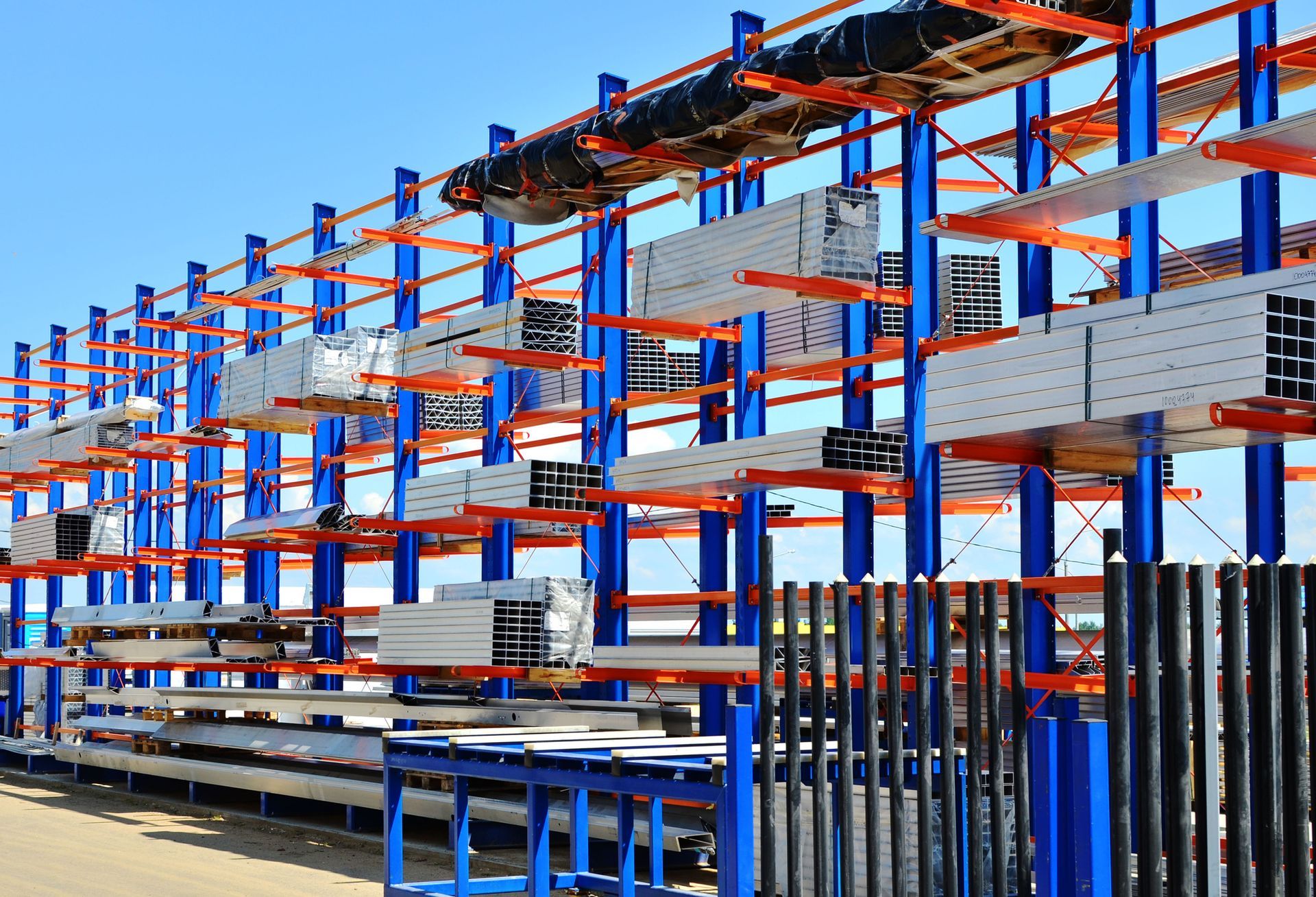 Blue and orange cantilever racking system holding metal beams and pipes outdoors.
