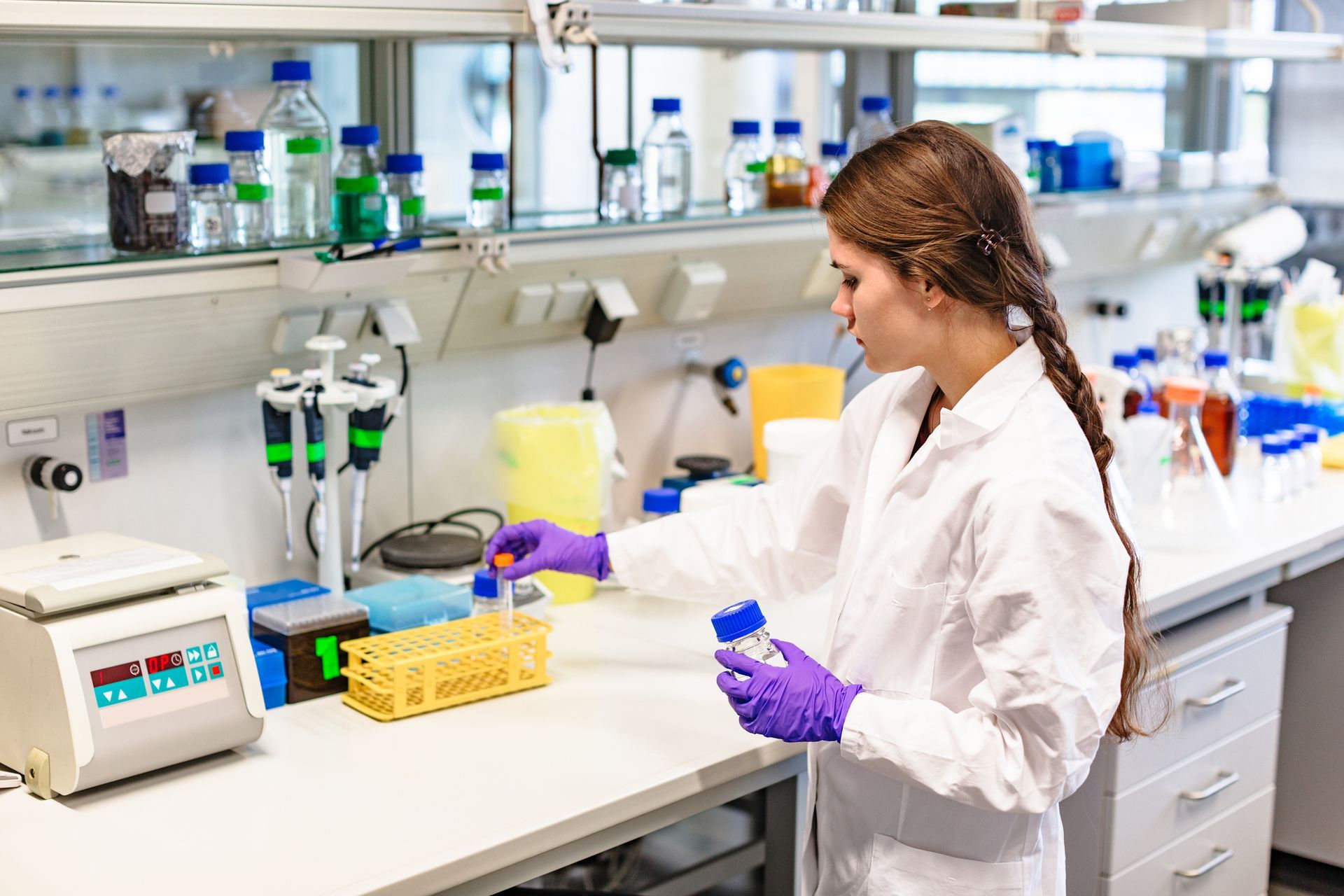 Woman in lab coat and gloves working with vials in a lab.