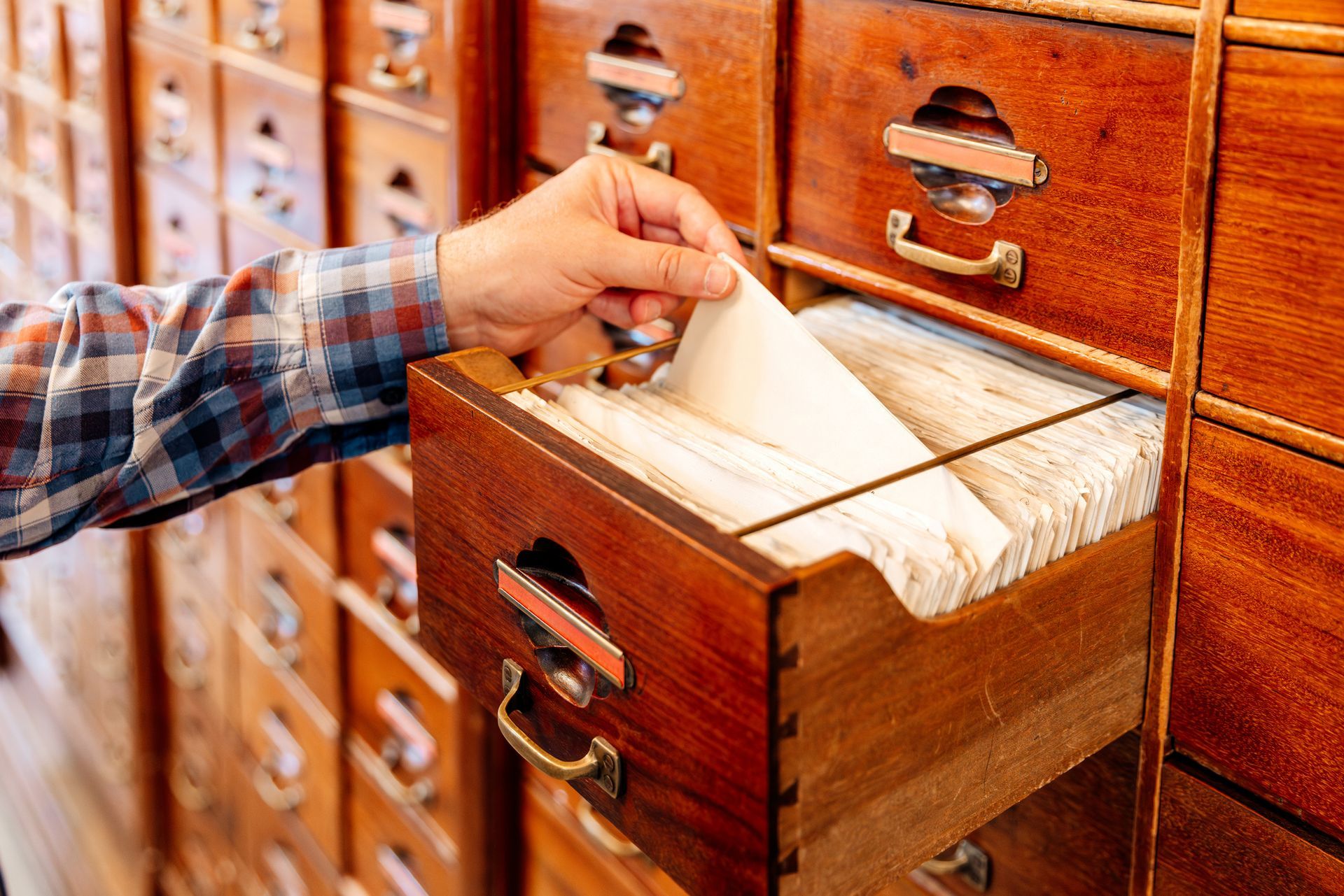 Hand reaching into a wooden drawer full of file cards, searching.
