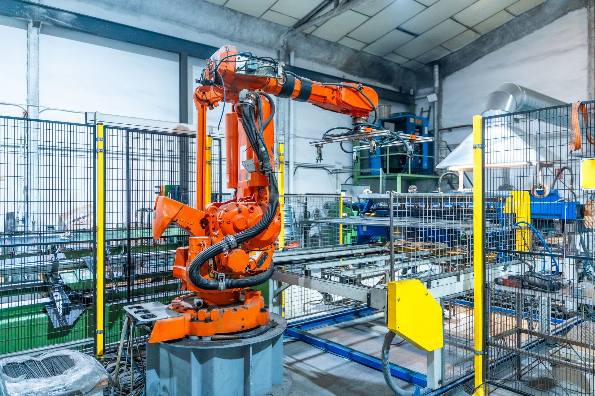 Orange industrial robot in a factory setting, working with other machinery and metal structures.
