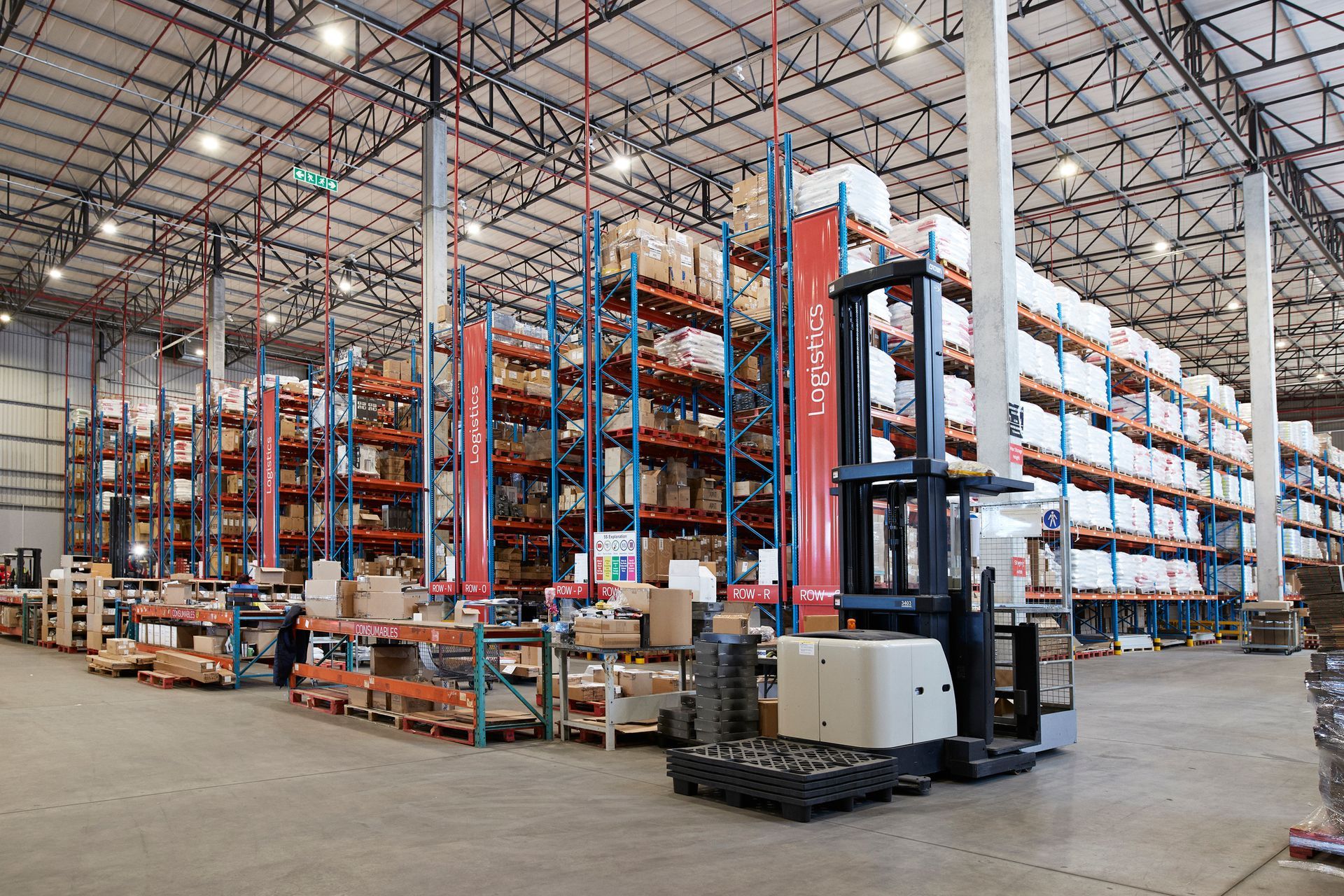 Warehouse interior with forklift, shelving filled with boxes, and overhead lighting.