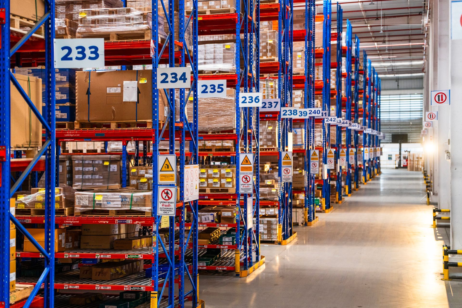 Warehouse interior with rows of blue and red shelving units, labeled with numbers, filled with inventory.