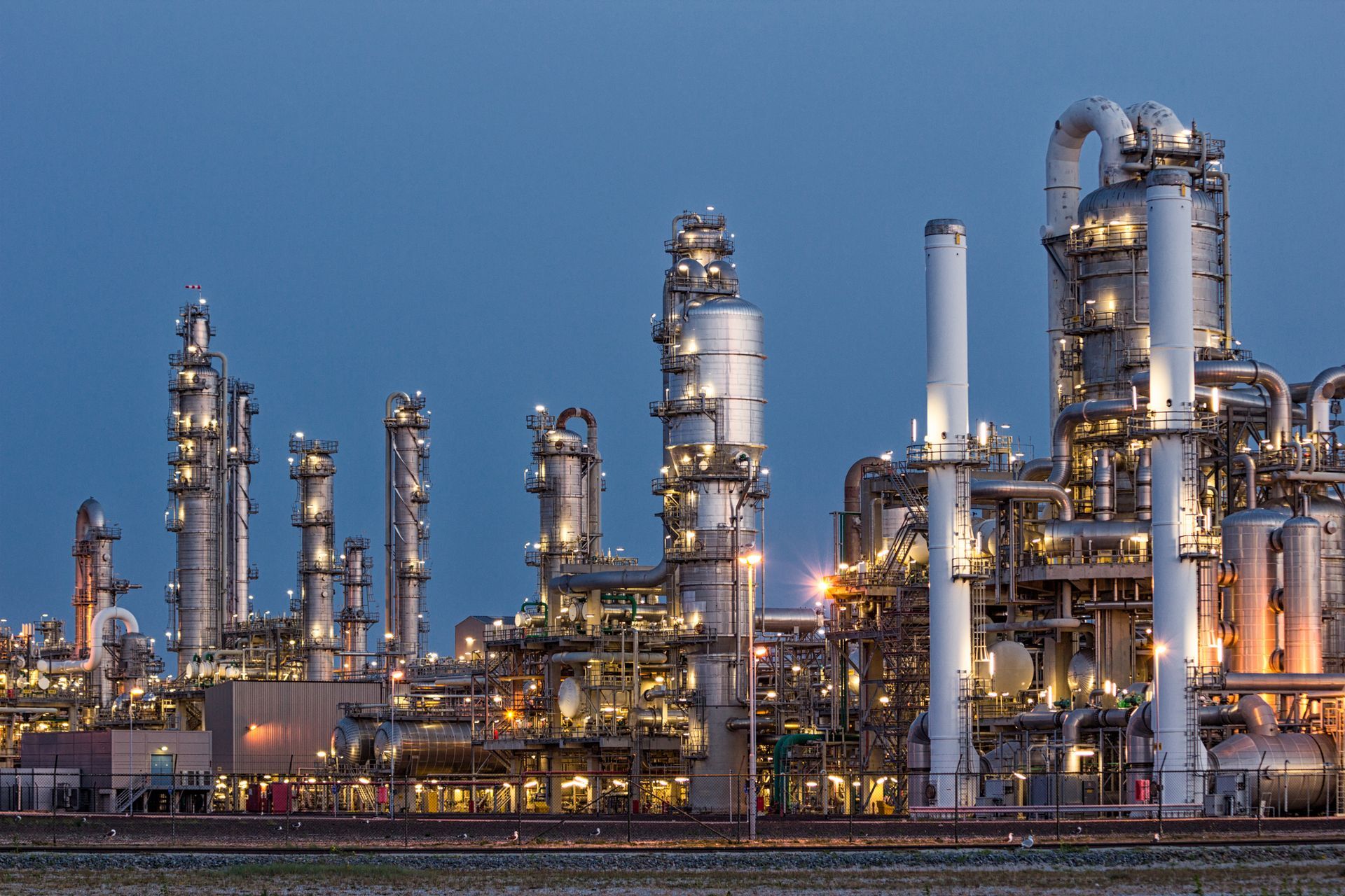 Oil refinery at dusk with illuminated towers and pipes.