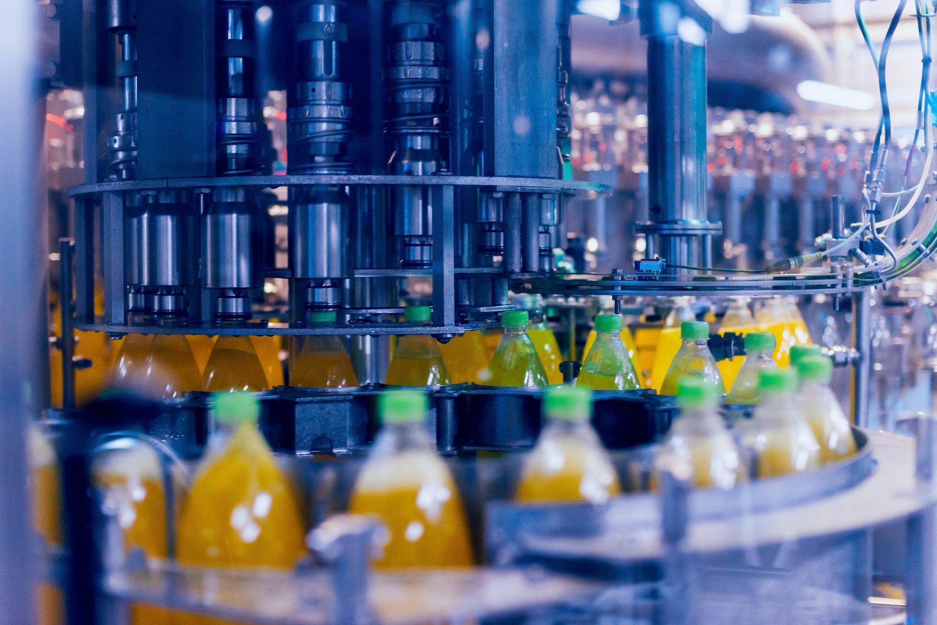 Bottling machine filling yellow liquid into clear bottles with green caps on an assembly line.