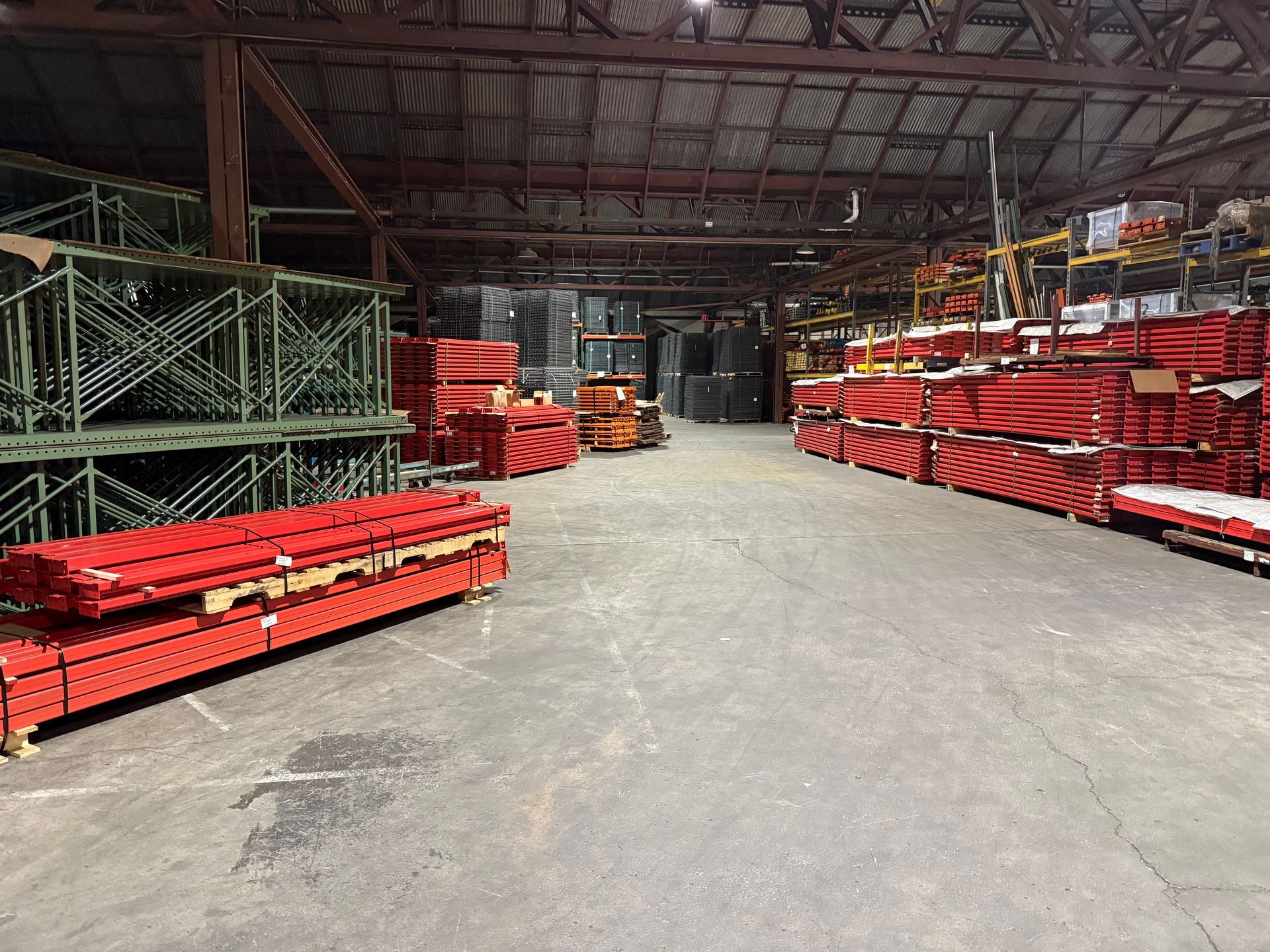 Warehouse worker with safety vest using a pallet jack to move boxes along a storage shelf.