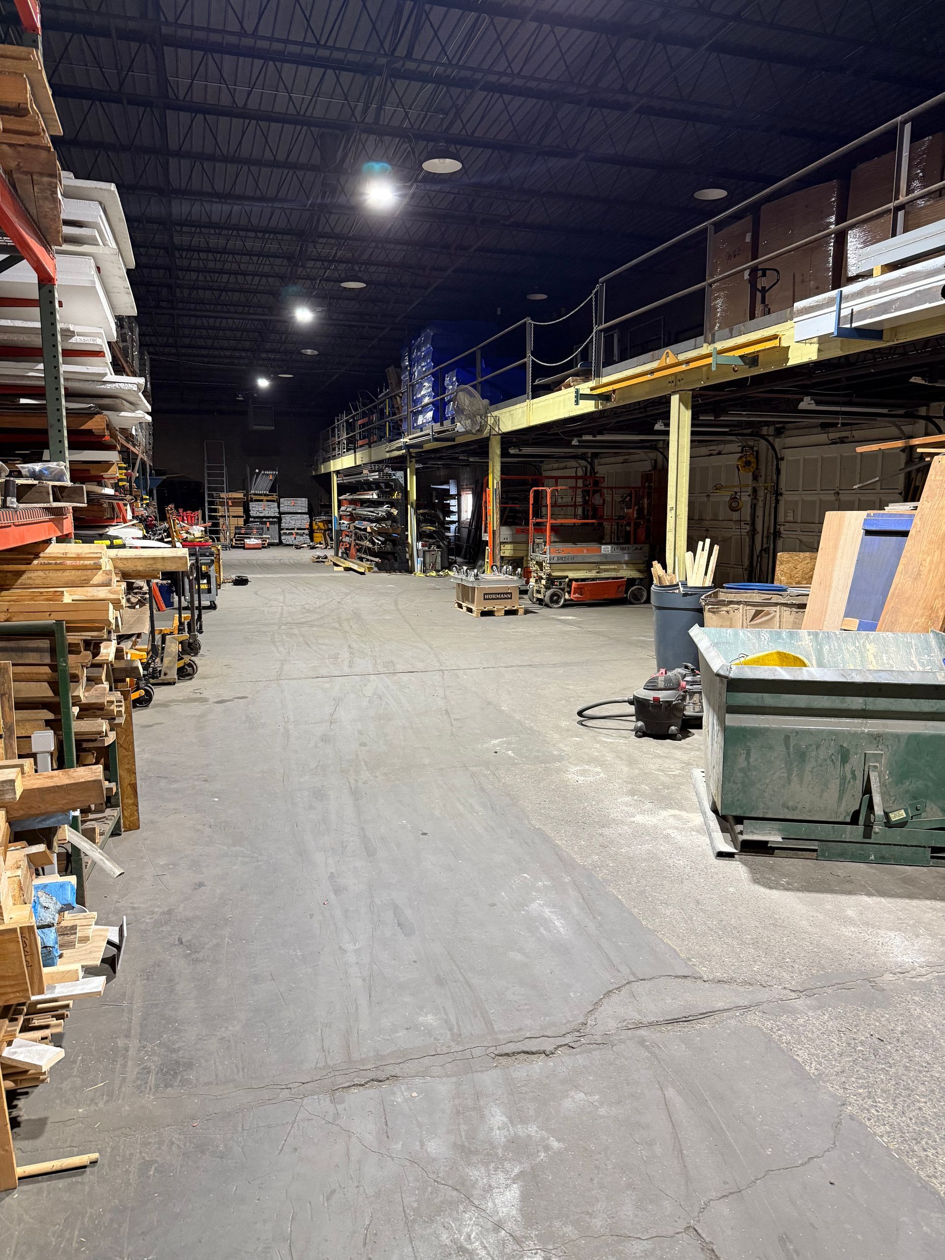 Warehouse worker in safety vest and hard hat, inspecting boxes on shelves with a tablet.