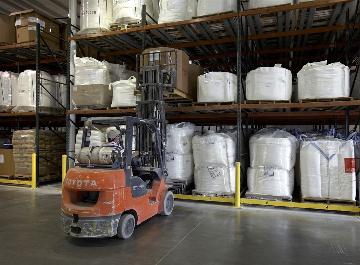 Red Toyota forklift in a warehouse, moving large bags of material stored on shelves. Red Toyota forklift in a warehouse, moving large bags of material stored on shelves.