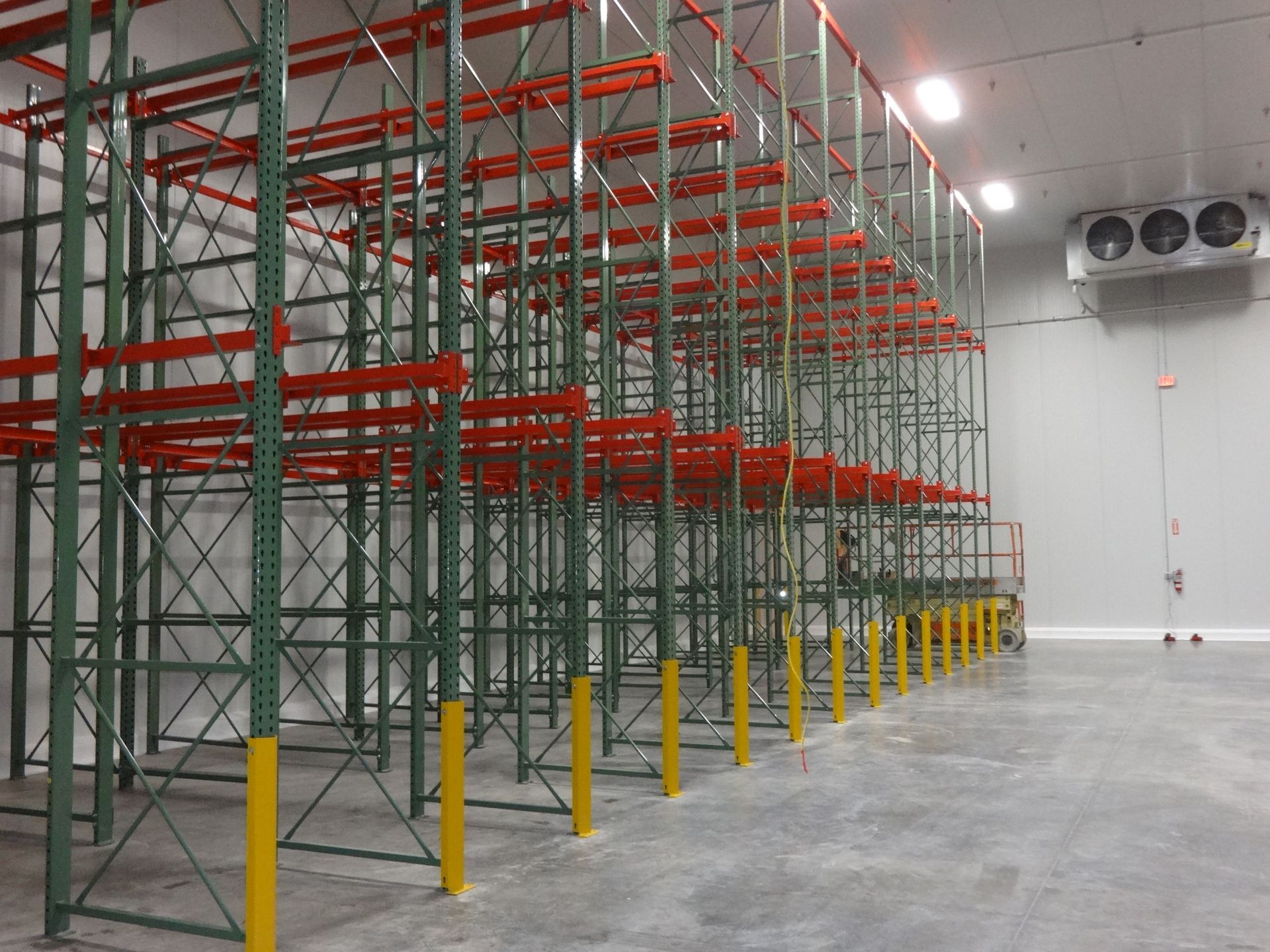 Empty warehouse with tall metal storage racks, yellow column protectors, and ceiling-mounted air conditioning units. Empty warehouse with tall metal storage racks, yellow column protectors, and ceiling-mounted air conditioning units.