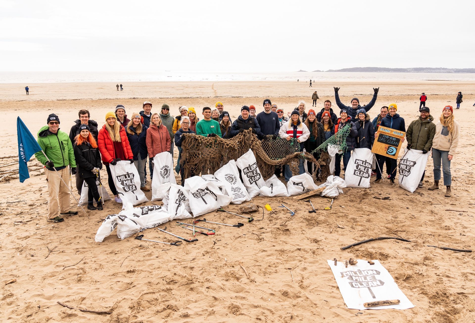 Man kayaking, smiling, with a group in kayaks on a choppy sea near rocky coast under a cloudy sky.