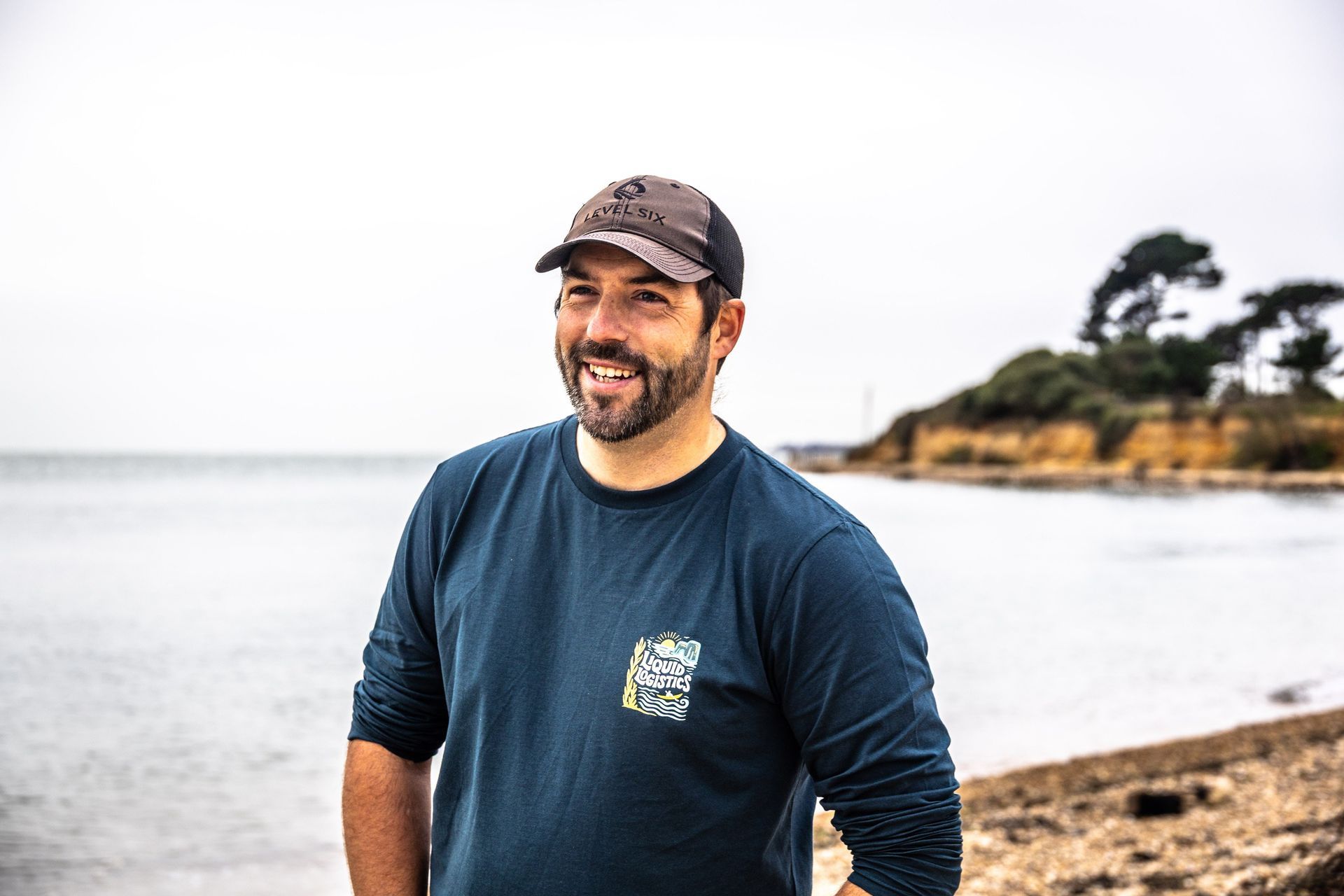 Man in yellow kayak smiles, paddling with group on water near rocky coast under cloudy sky.