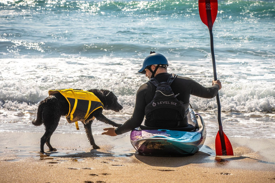 Woman paddles a colorful canoe on a lake, smiling, wearing a hat and life vest.