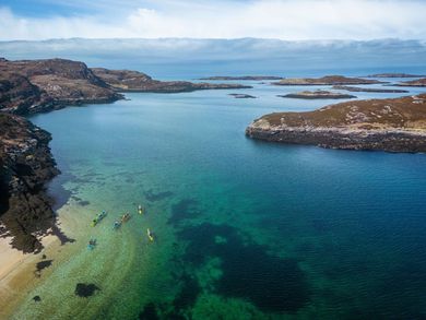 Kayakers in turquoise water near rocky islands, under a cloudy sky.