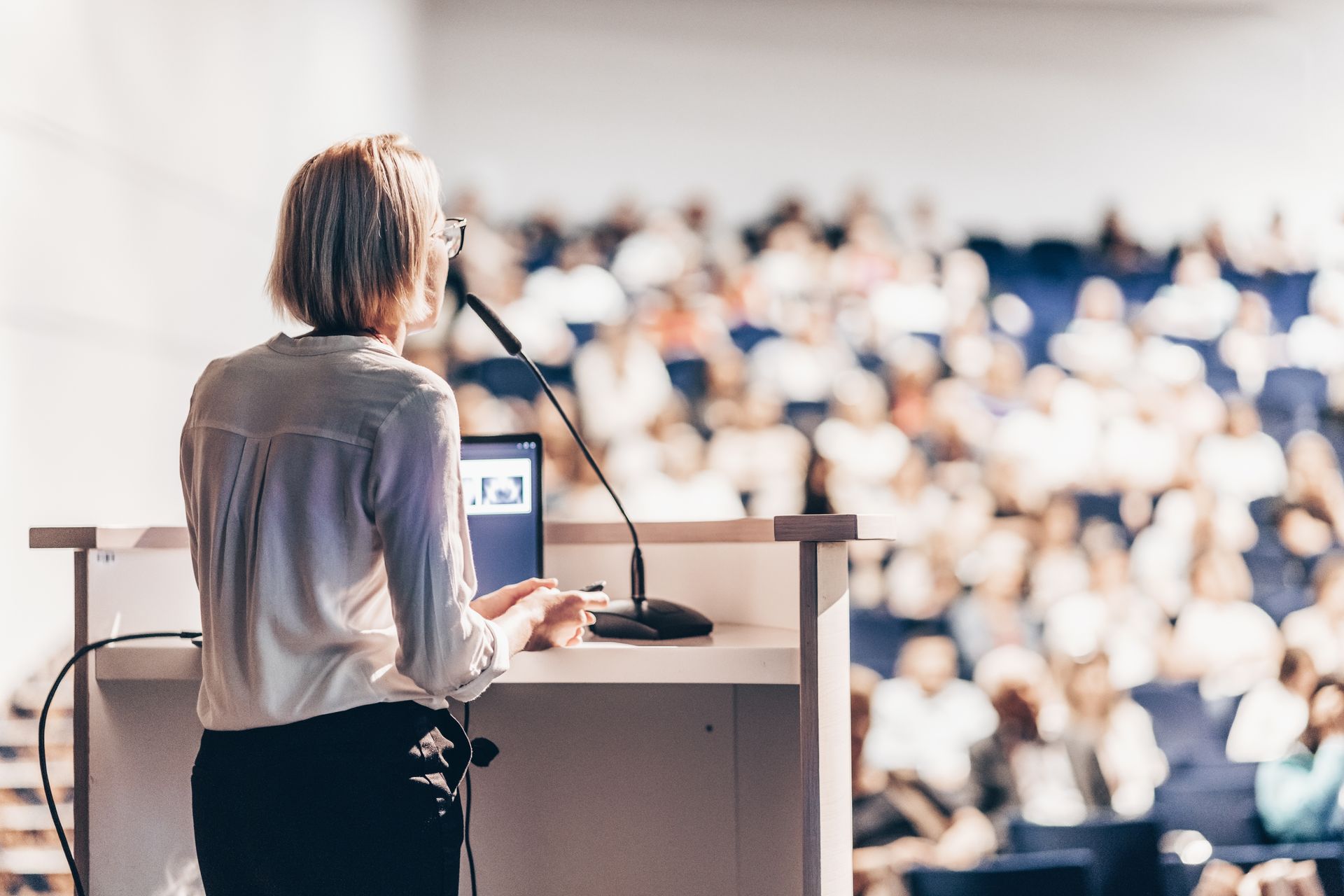 A woman is giving a speech at a podium in front of a crowd.