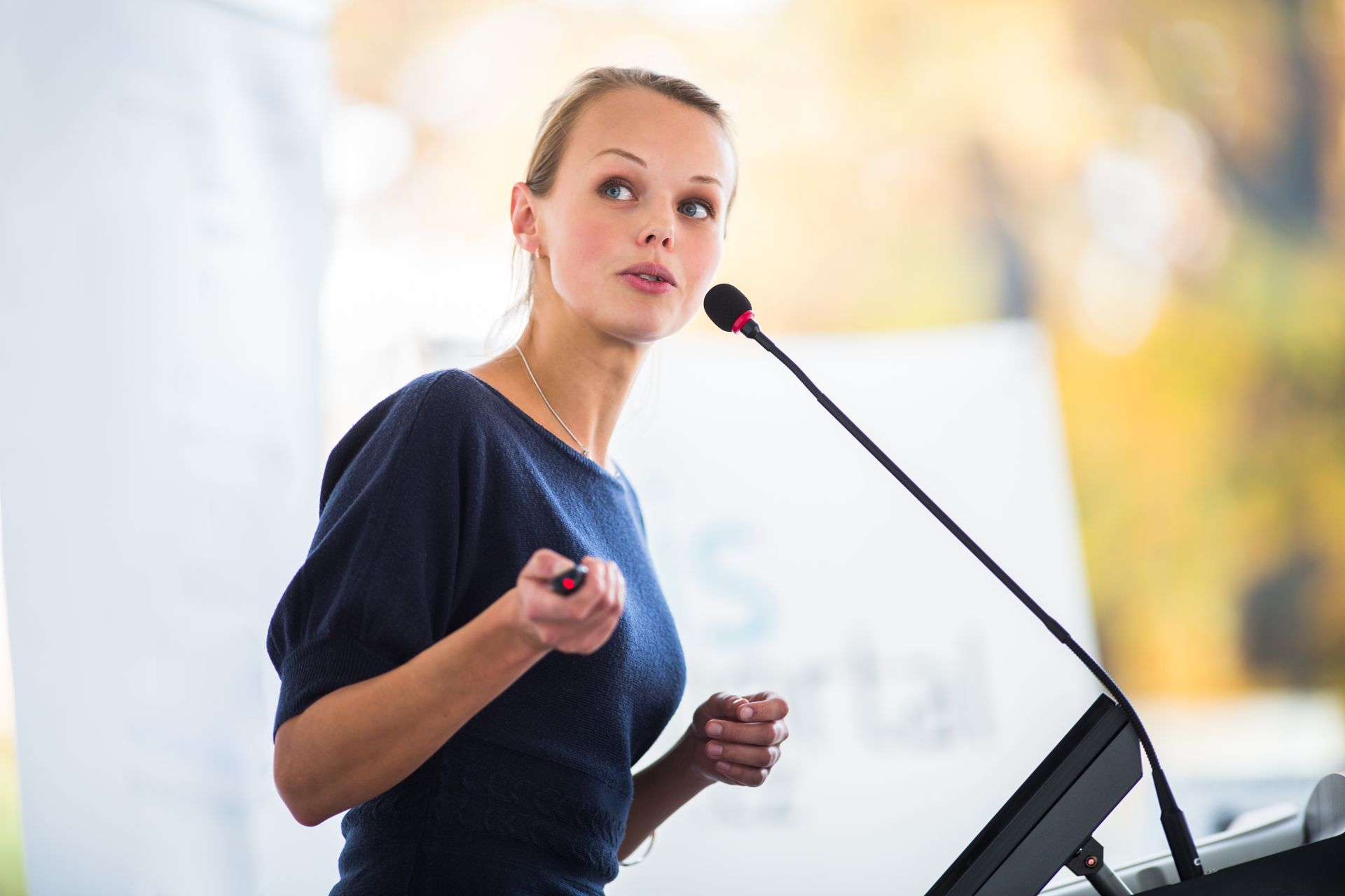 A woman is giving a speech at a podium in front of a microphone.