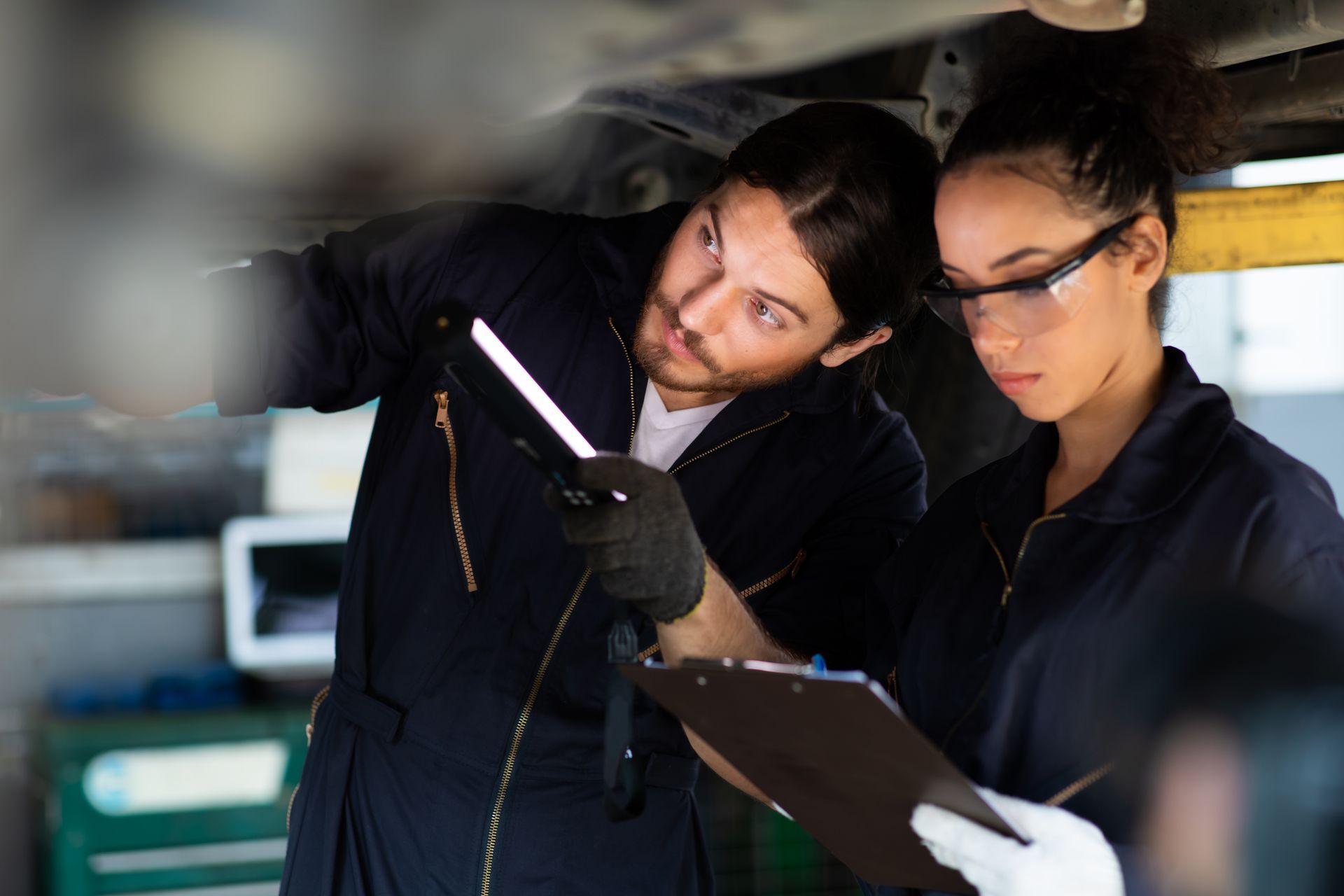 A man and a woman are working on a car in a garage.
