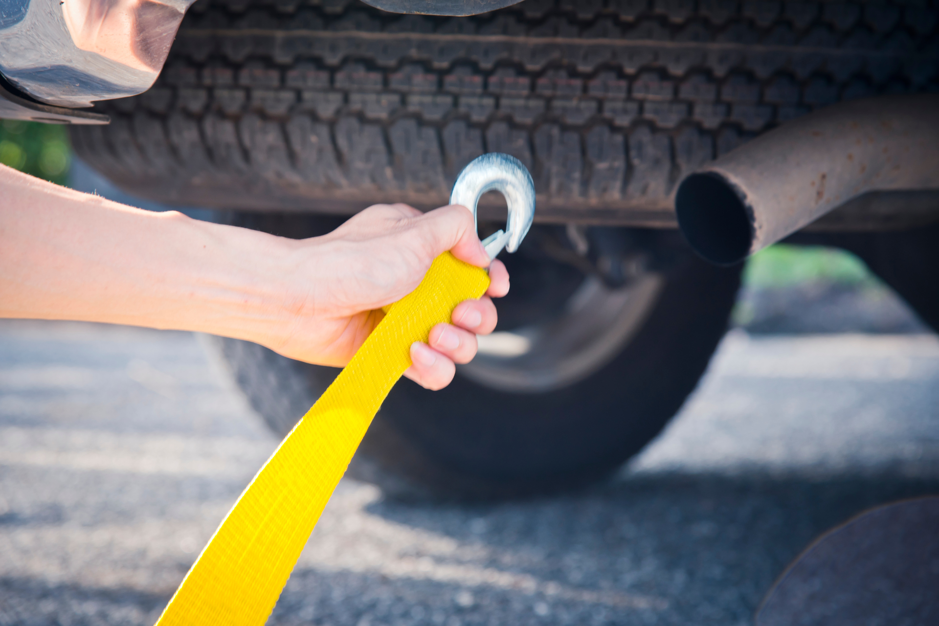 Hand holding a yellow tow strap attached to a vehicle's undercarriage.