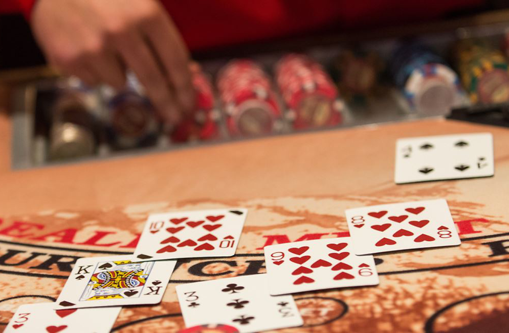 Poker table with dealt cards: King, eight, and nine of hearts, and a six of diamonds. Red poker chips in background.