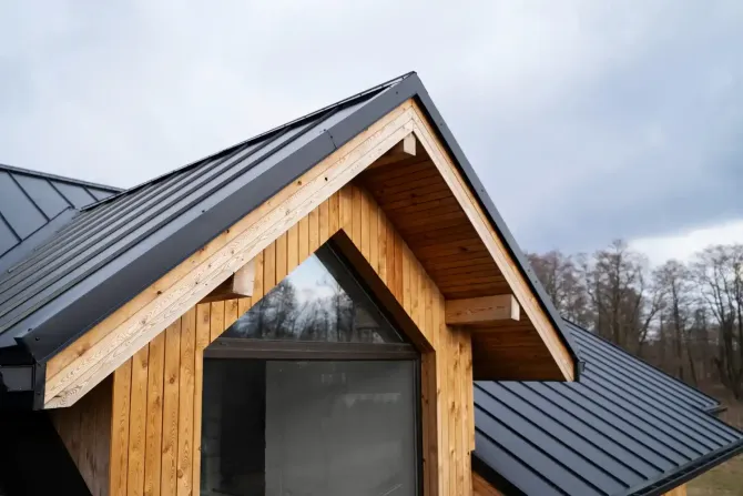 Wooden cabin with a dark gray metal roof against a cloudy sky.