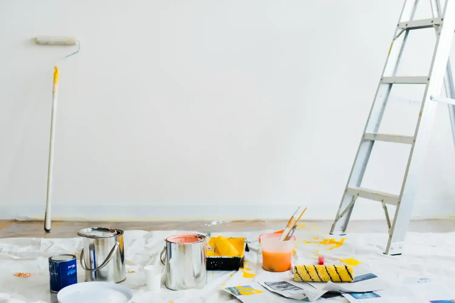 Paint supplies on drop cloth in room with ladder and half-painted wall.