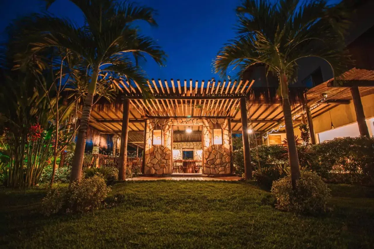 Uma casa com uma pérgola e palmeiras no quintal à noite. Pousada-Ocacocar