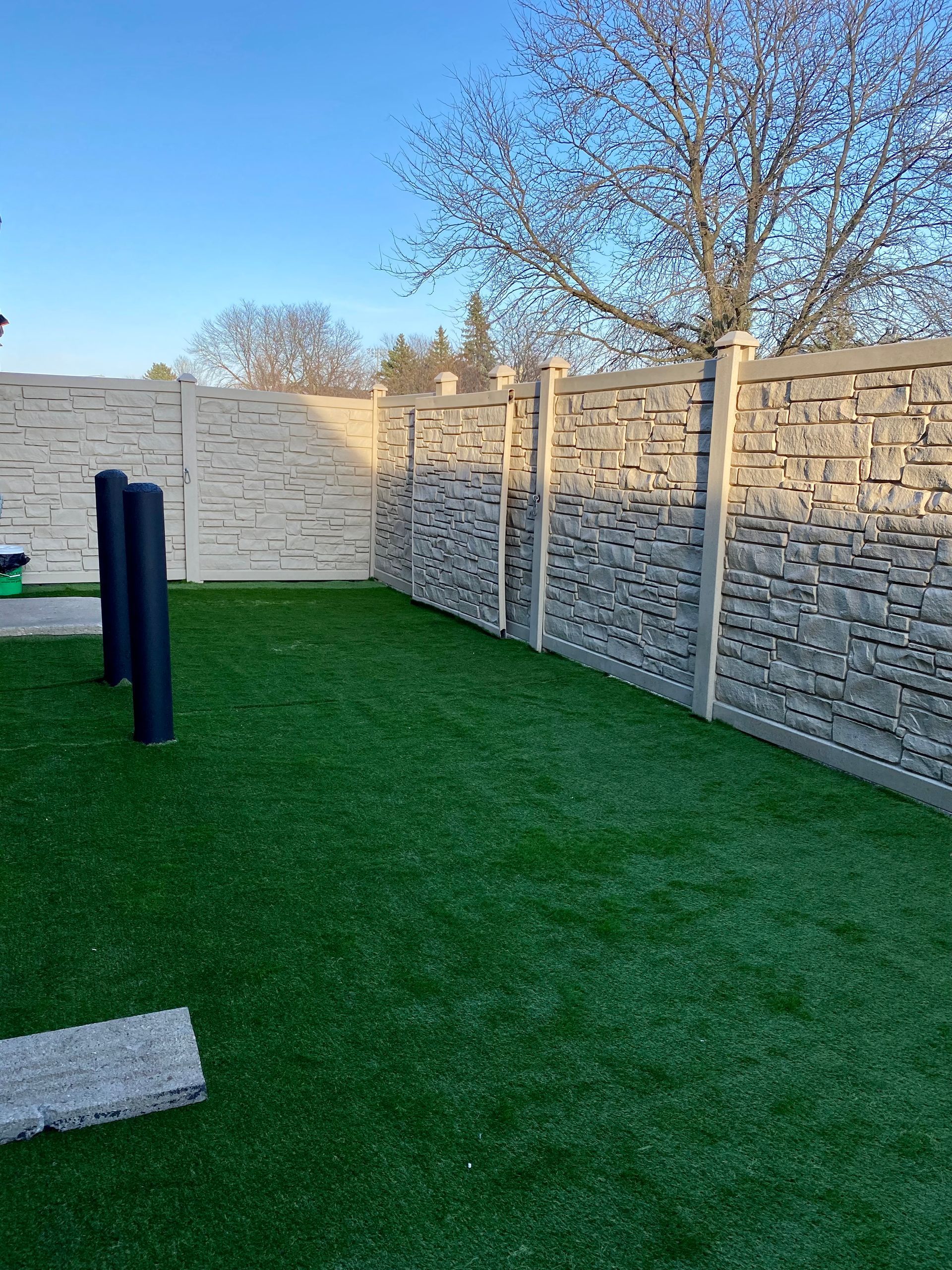 A backyard with a stone fence and a lush green lawn.