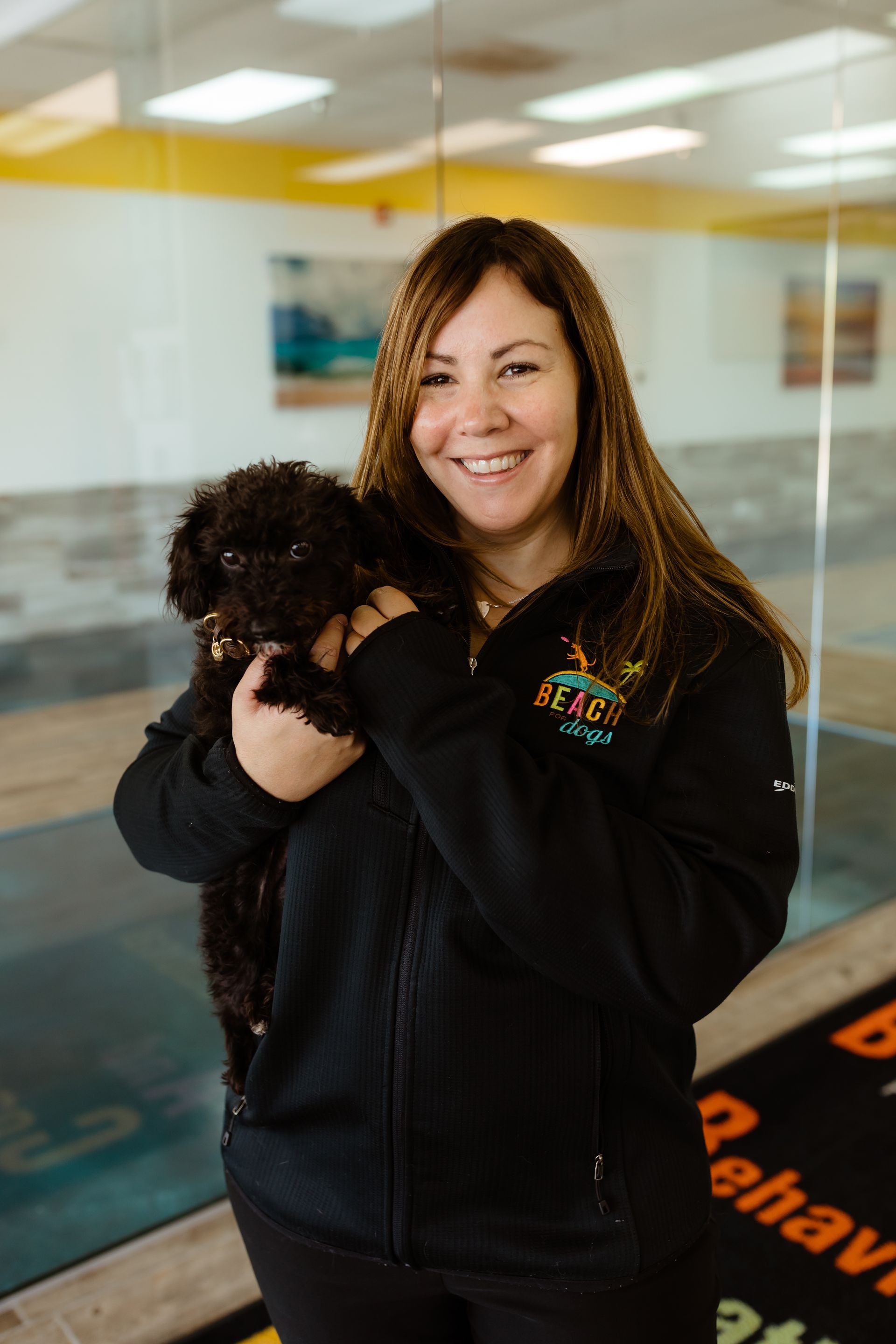 A woman is holding a small black dog in her arms.