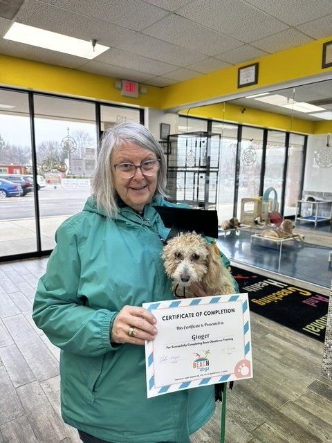 A woman in a green jacket is holding a dog and a certificate of completion.