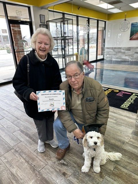 A man and a woman are holding a certificate and posing with a dog.