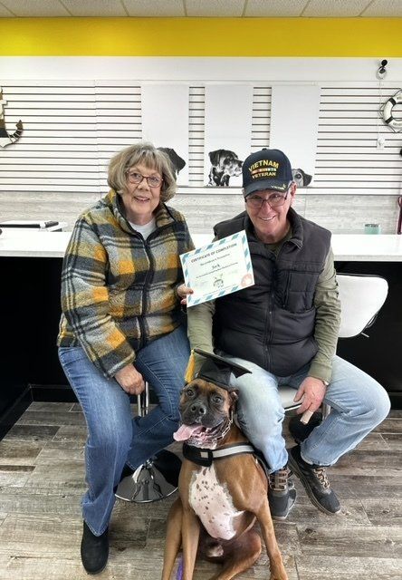 A man and a woman are sitting next to a dog and holding a certificate.