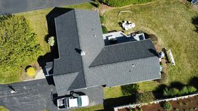 Overhead view of a house with a dark gray roof, black asphalt driveway, and green lawn. White truck parked.