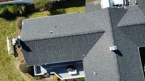 Overhead view of a house with a dark gray shingled roof, a small patio, and a vehicle in the driveway.