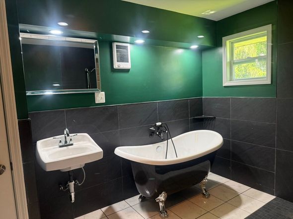 Bathroom with a claw-foot tub, black and white tile, a white sink, and dark green walls.