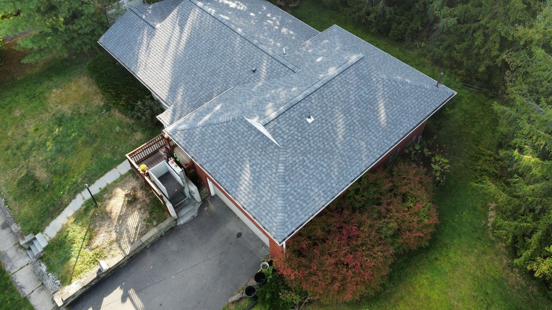 Aerial view of a gray-roofed house with a red bush in the front yard and a paved driveway.