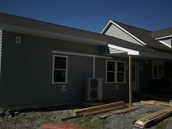 Gray-sided building with dark roof under construction; windows and an HVAC unit are visible.