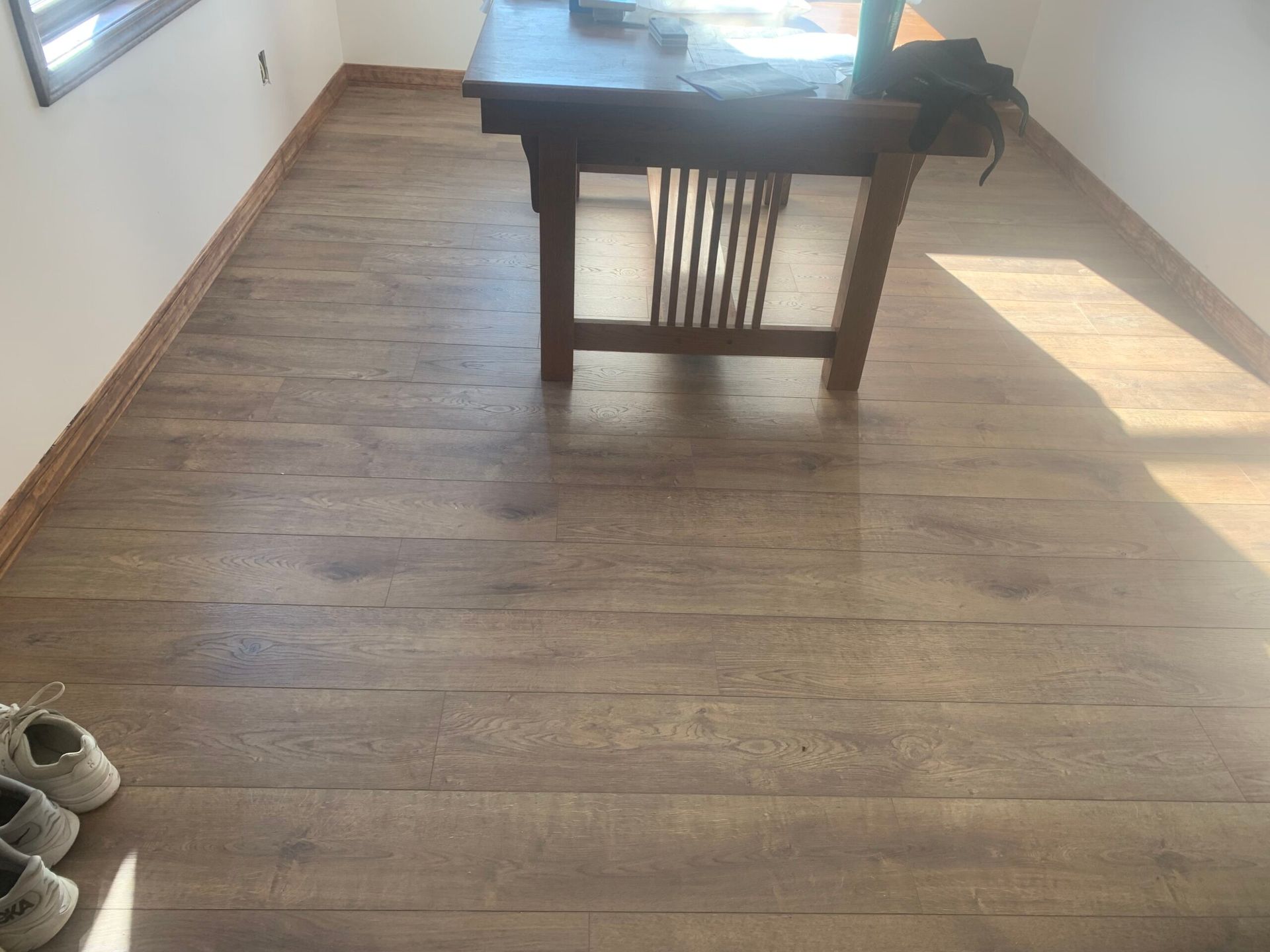 Wooden floors with a dark brown table and white walls in a sunny room.