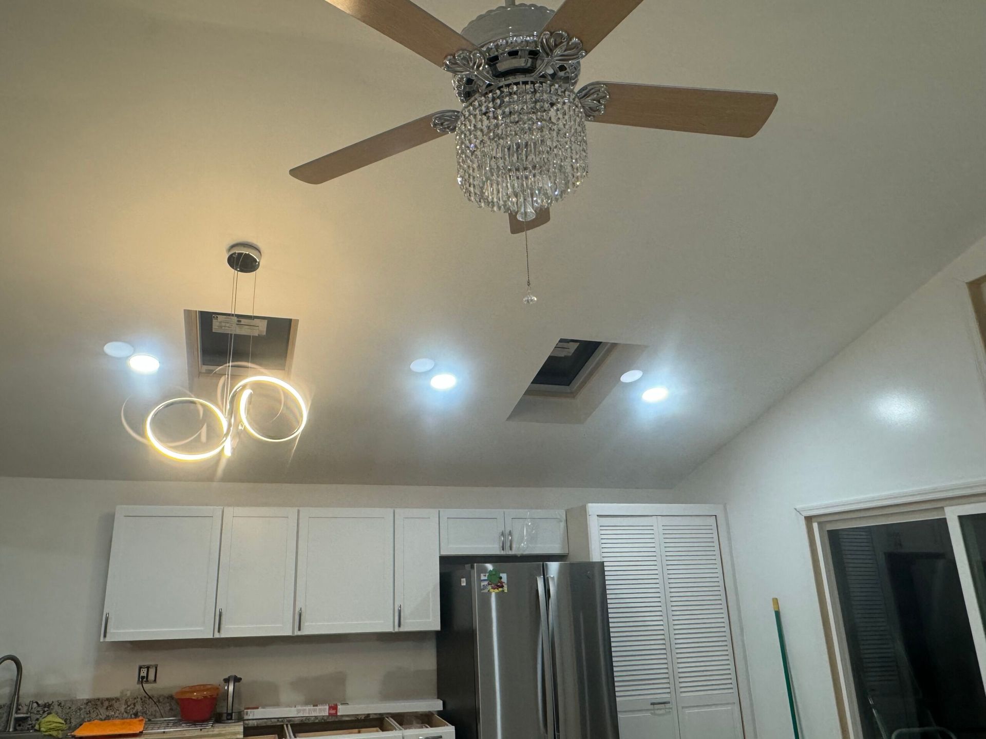 Kitchen ceiling with ceiling fan, chandelier, recessed lights, and exposed wiring.
