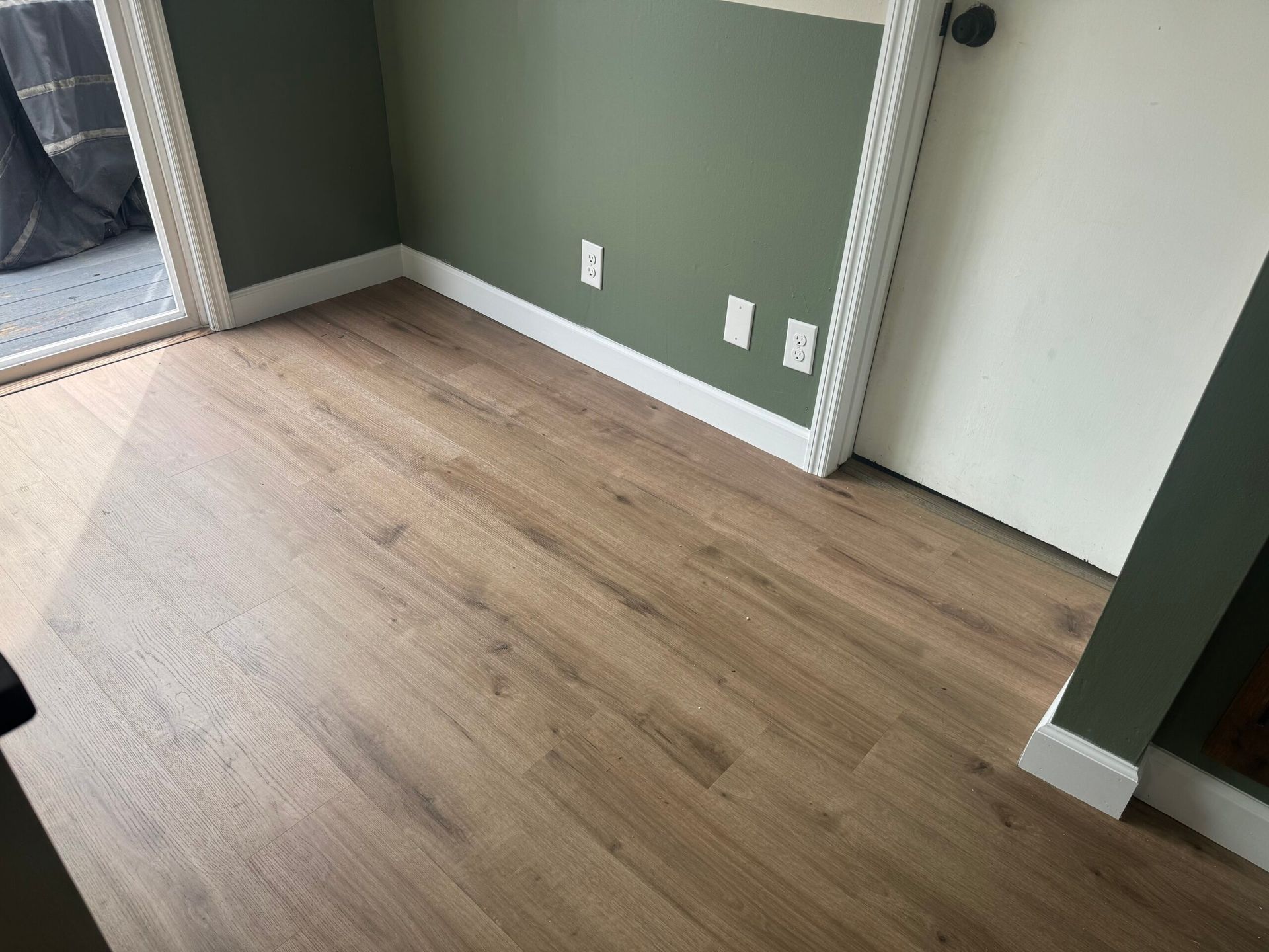 Room with wood-look flooring, green walls, white trim, and a closed white door.