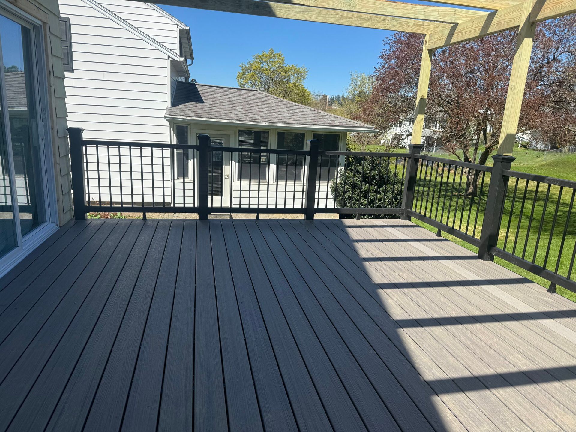 A composite deck with black railing and pergola, sunny outdoors, house in background.
