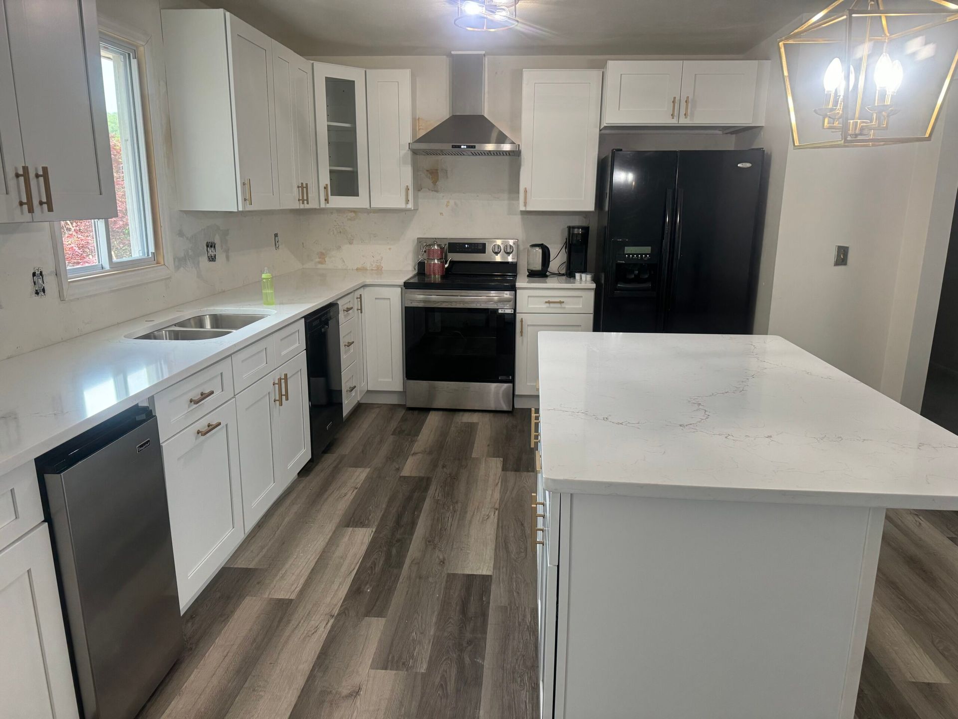 White kitchen with stainless steel appliances, white countertops, and wood-look flooring.