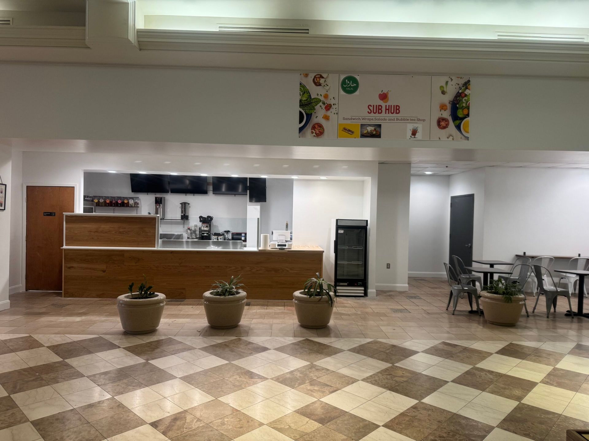 Empty cafe interior with wood counter, potted plants, checkered floor, and tables.