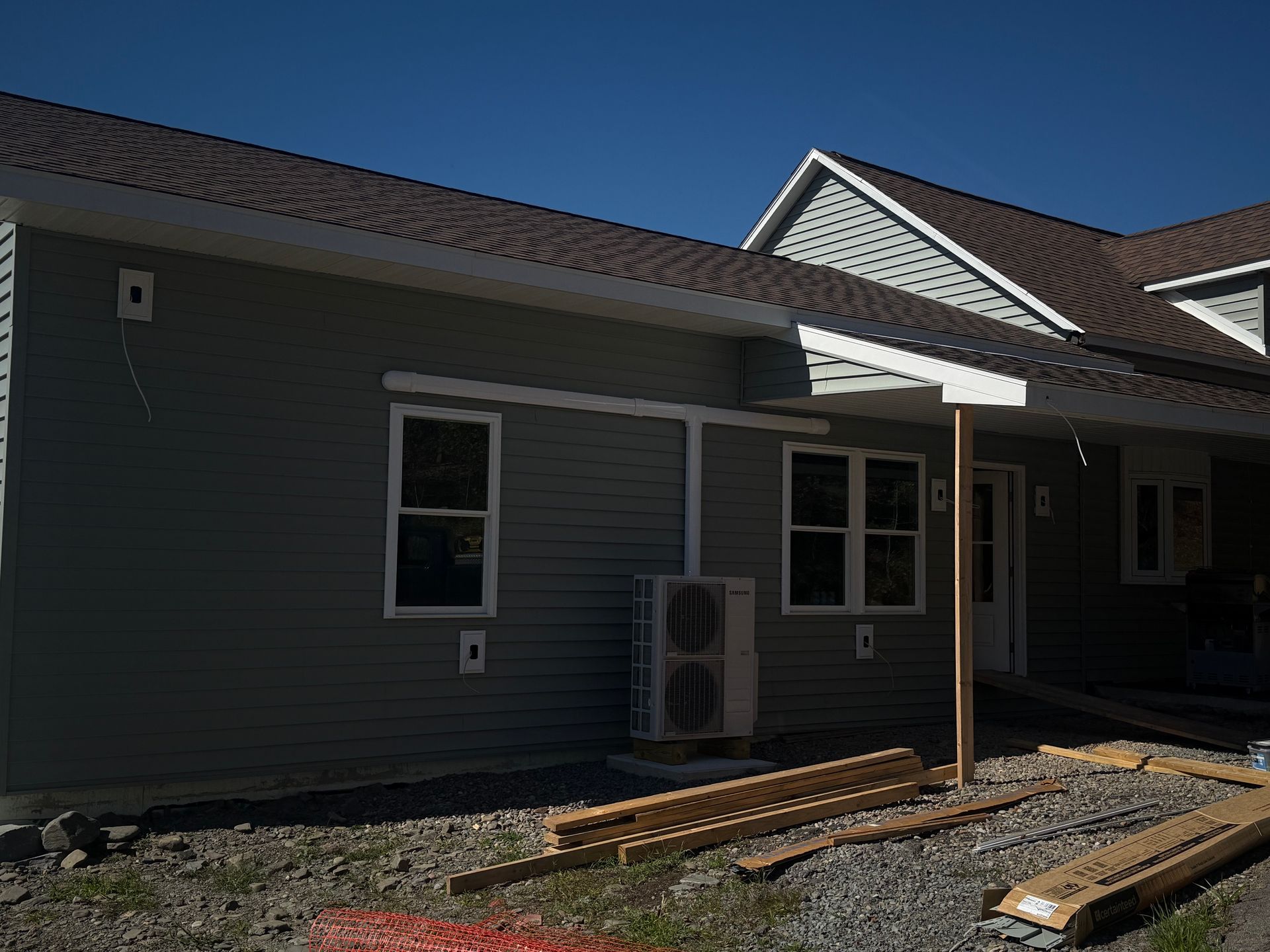 Gray siding building with brown roof, windows, and an air conditioning unit. Construction materials are in the foreground.