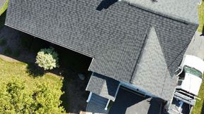 Overhead view of a house with a dark gray shingled roof, a white truck, and surrounding greenery.