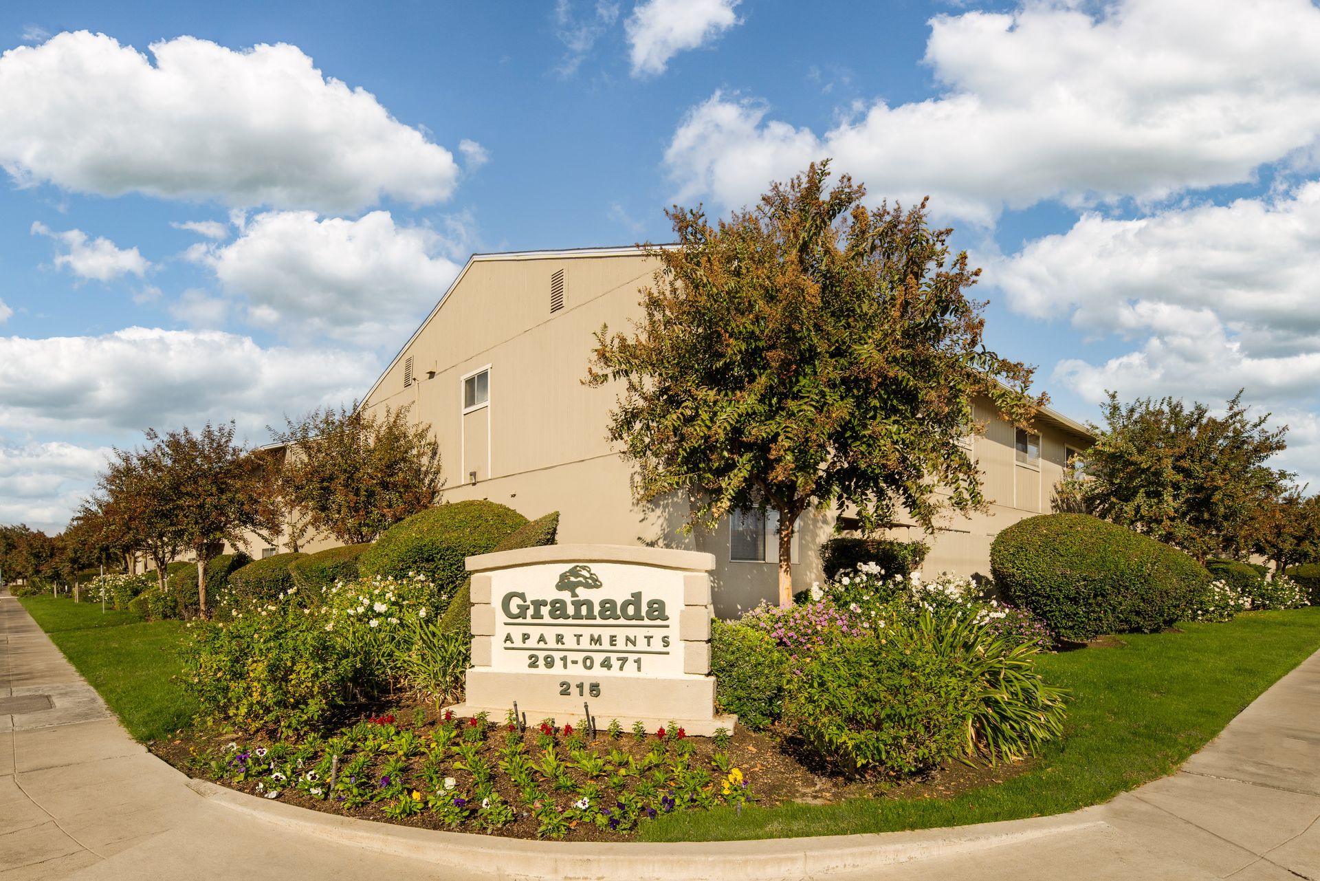 Granada Apartments sign in front of a beige building surrounded by landscaping under a blue sky.