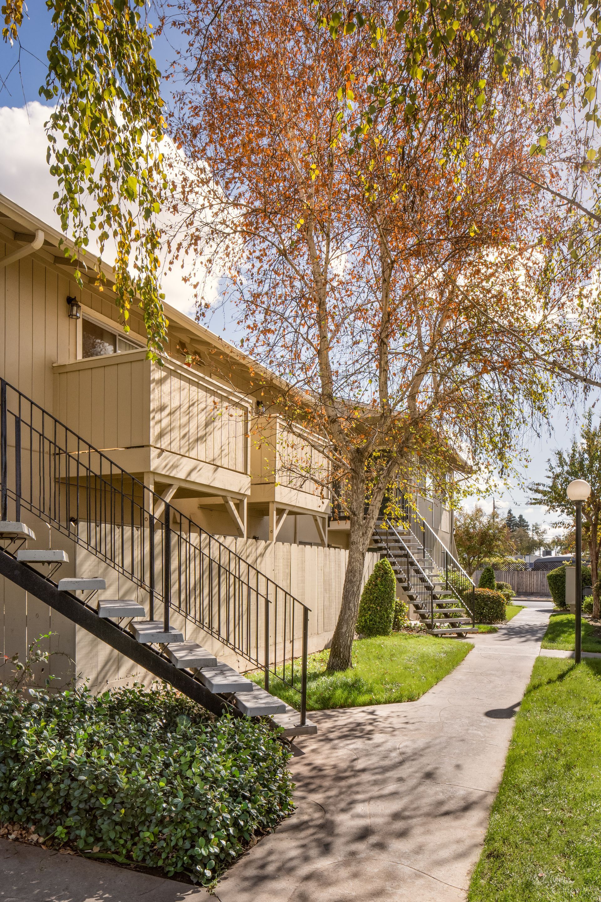Apartment building with beige walls and black staircases, walkway, and trees with fall foliage.