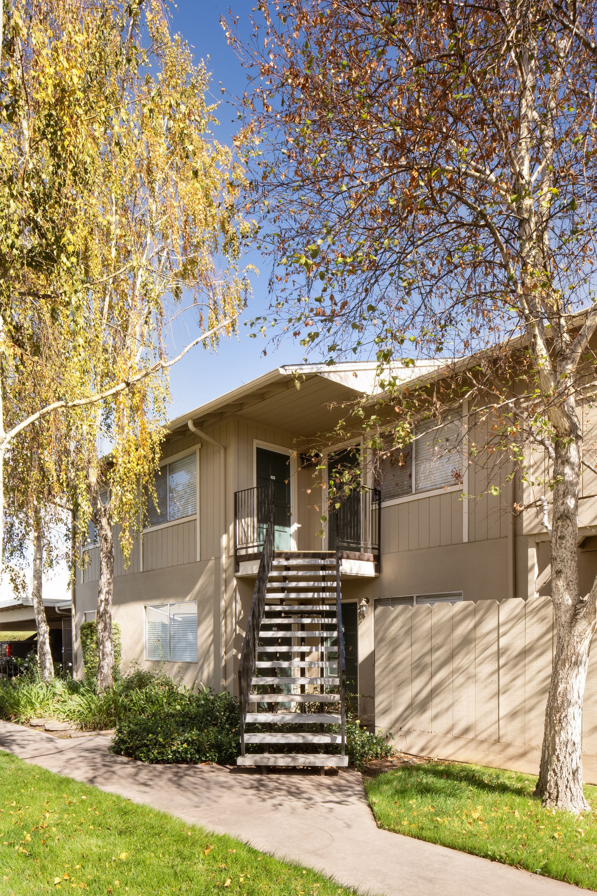Two-story apartment building with exterior stairs, trees, and green lawn.