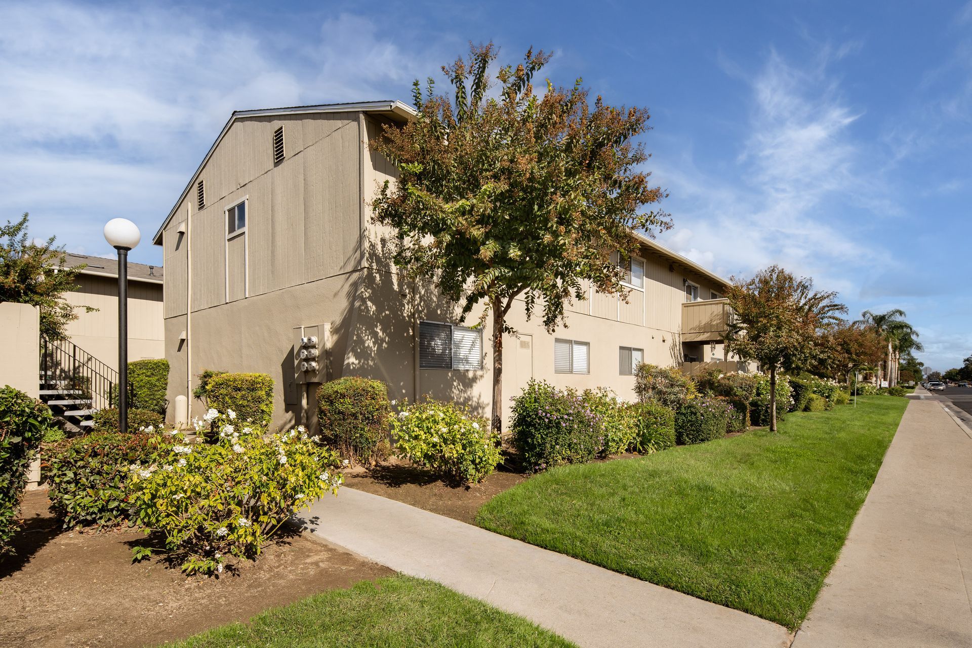 Beige two-story apartment building with landscaping and a sidewalk on a sunny day.