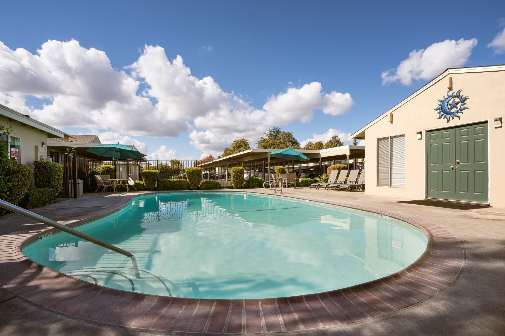 A swimming pool surrounded by brick and buildings on a sunny day with clouds.