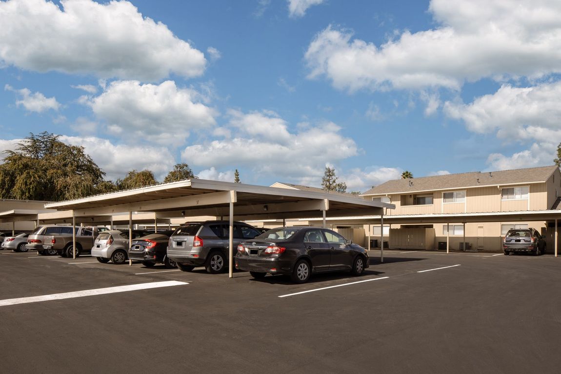 Cars parked under a carport in an apartment complex on a sunny day.